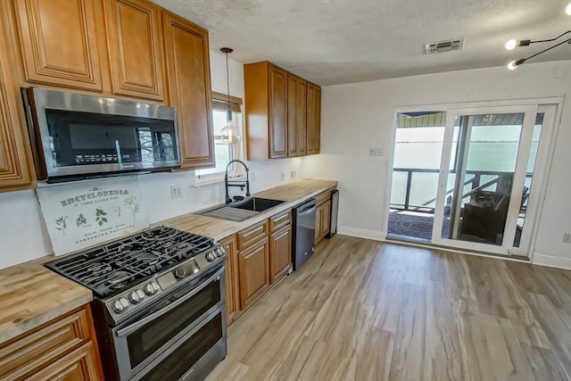 kitchen with light wood-style flooring, a sink, visible vents, wooden counters, and appliances with stainless steel finishes