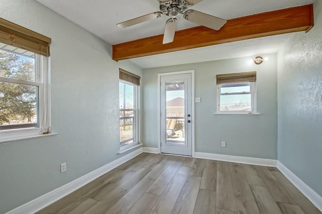 doorway with baseboards, beamed ceiling, light wood finished floors, and ceiling fan