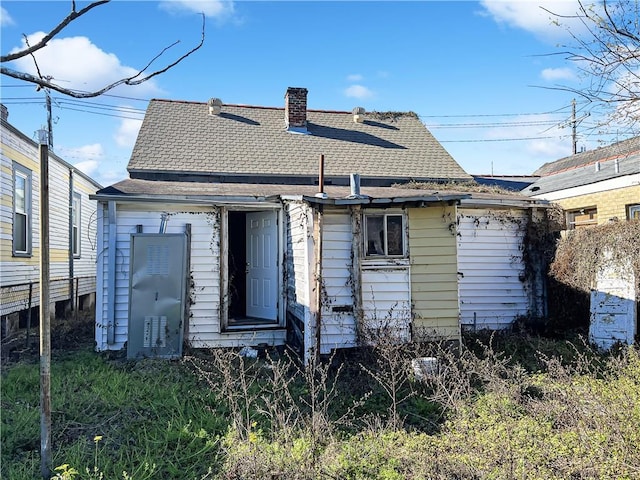 back of house with roof with shingles and a chimney