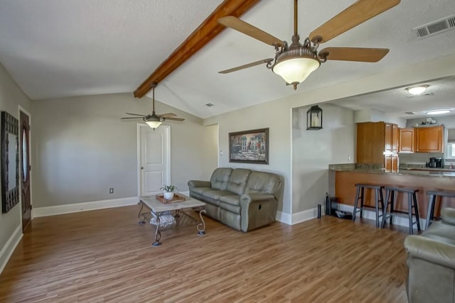 living area with vaulted ceiling with beams, baseboards, visible vents, and wood finished floors