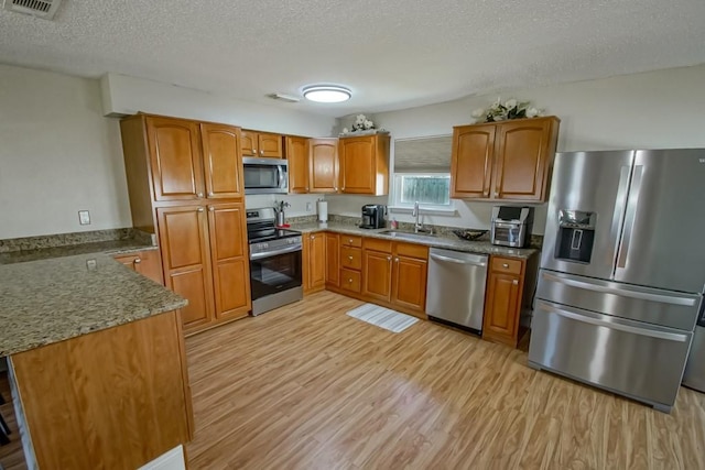 kitchen with stainless steel appliances, light wood-type flooring, brown cabinetry, and a sink