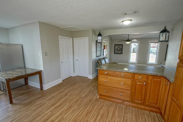 kitchen with stone countertops, visible vents, baseboards, light wood-style flooring, and brown cabinets