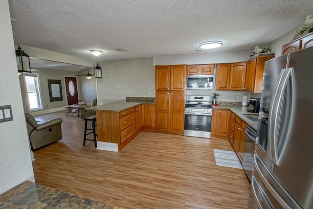 kitchen with a peninsula, appliances with stainless steel finishes, a breakfast bar area, and brown cabinets