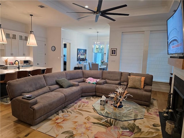 living room with light wood finished floors, visible vents, a fireplace with raised hearth, and ceiling fan with notable chandelier