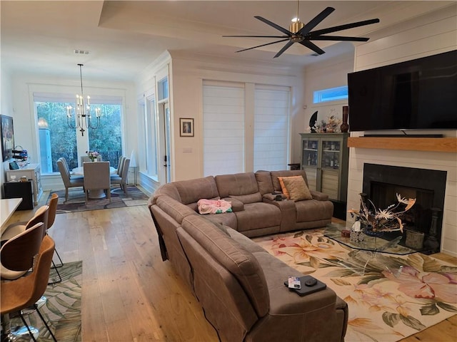 living room with light wood-style flooring, ceiling fan with notable chandelier, a fireplace, visible vents, and ornamental molding