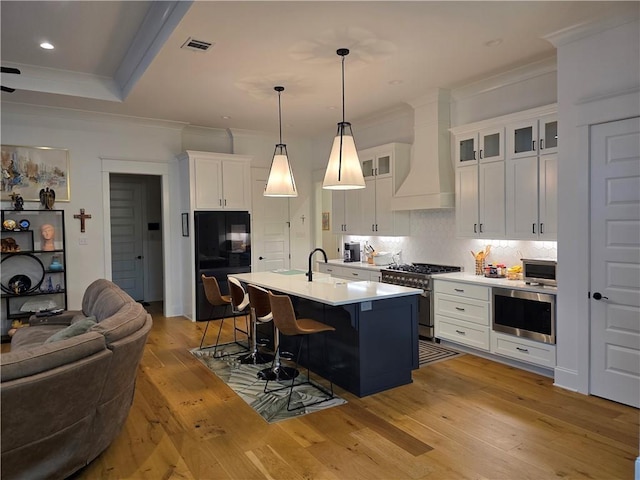 kitchen featuring visible vents, premium range hood, decorative backsplash, appliances with stainless steel finishes, and a kitchen breakfast bar