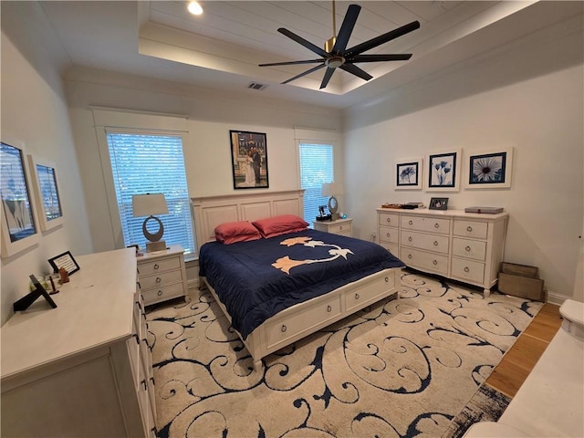 bedroom featuring a raised ceiling, light wood-style flooring, multiple windows, and visible vents