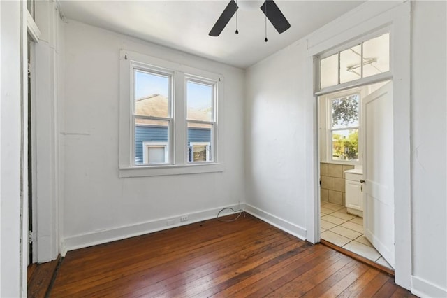 unfurnished bedroom with dark wood-style floors, multiple windows, baseboards, and connected bathroom