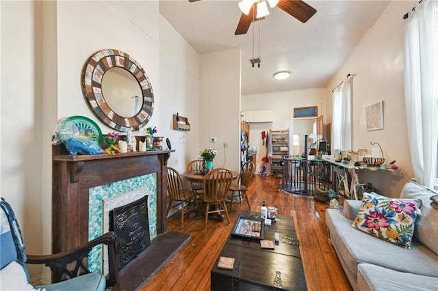 living room with a fireplace with raised hearth, ceiling fan, and hardwood / wood-style floors