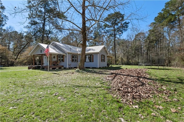 view of front of home with covered porch, metal roof, a trampoline, and a front yard