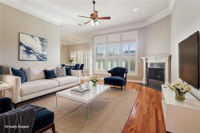 living area with crown molding, light wood finished floors, a ceiling fan, a tile fireplace, and baseboards