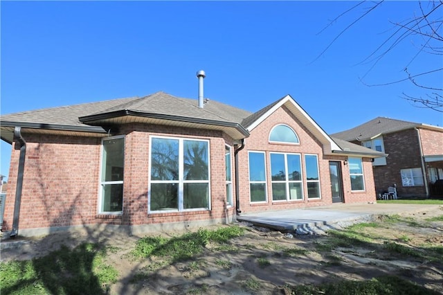 rear view of house with a patio area, roof with shingles, and brick siding