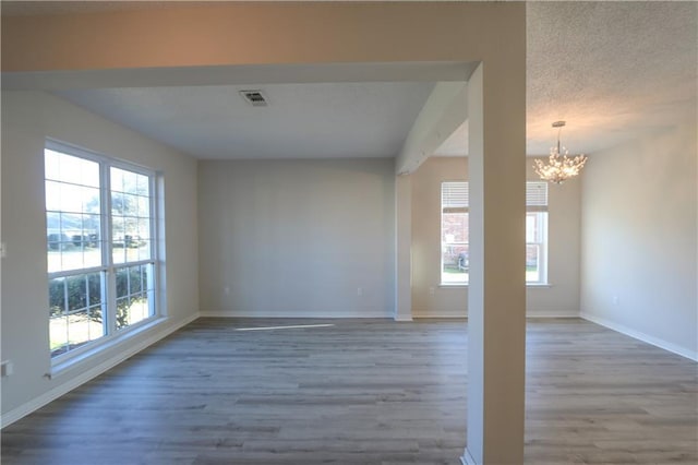 spare room featuring baseboards, visible vents, a chandelier, and wood finished floors