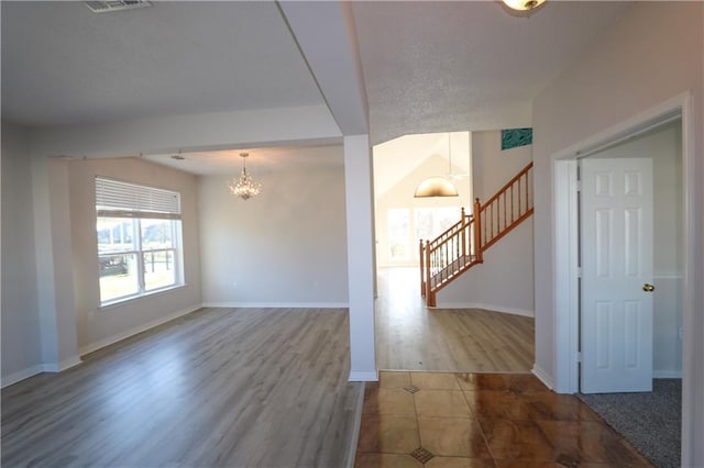 empty room with wood finished floors, stairway, baseboards, and an inviting chandelier