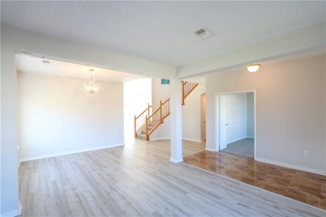 empty room featuring visible vents, an inviting chandelier, wood finished floors, baseboards, and stairs