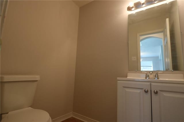 half bathroom with baseboards, vanity, and toilet