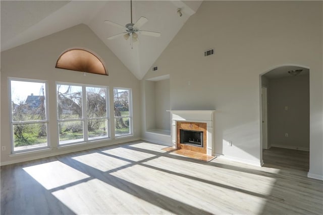 unfurnished living room featuring arched walkways, a fireplace, visible vents, a ceiling fan, and wood finished floors