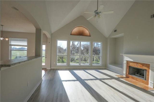 unfurnished living room featuring a tile fireplace, visible vents, arched walkways, and wood finished floors