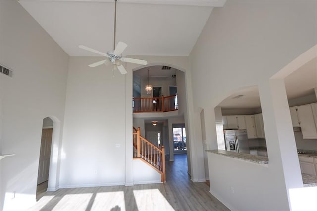 interior space with light wood finished floors, arched walkways, a ceiling fan, a towering ceiling, and stairs