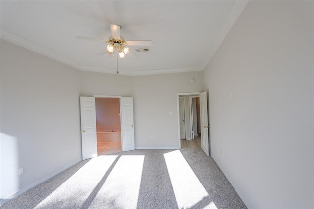 unfurnished bedroom featuring baseboards, visible vents, light colored carpet, ensuite bath, and crown molding