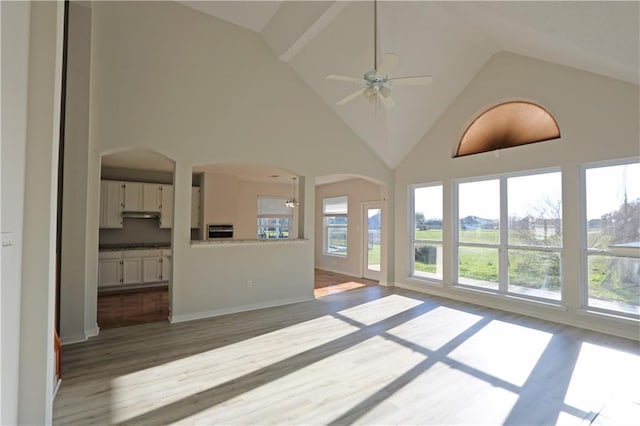 unfurnished living room featuring ceiling fan, high vaulted ceiling, arched walkways, and wood finished floors