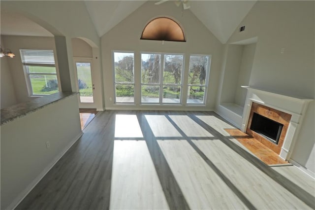 unfurnished living room featuring baseboards, visible vents, arched walkways, wood finished floors, and a fireplace