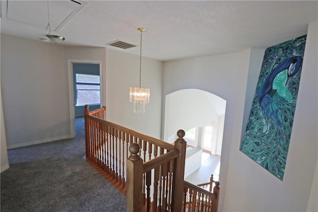 hall with attic access, visible vents, carpet flooring, an upstairs landing, and a notable chandelier