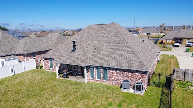 rear view of property featuring brick siding, a shingled roof, a lawn, central AC, and a fenced backyard