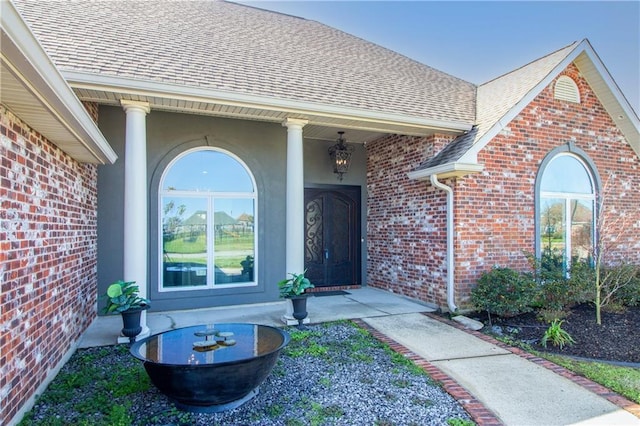 property entrance featuring a shingled roof, brick siding, and stucco siding