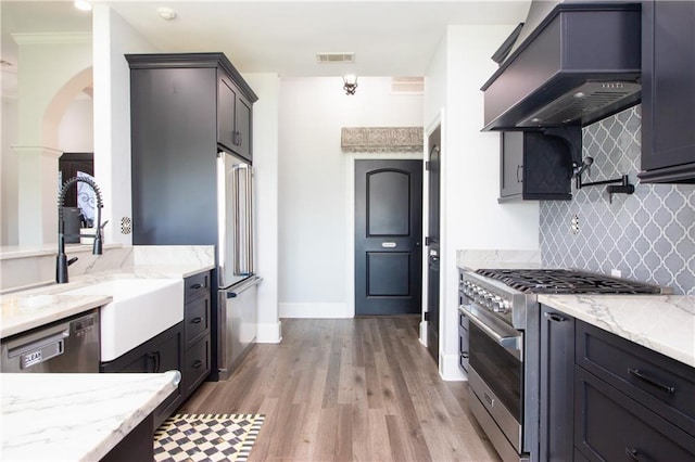 kitchen featuring high end appliances, custom range hood, visible vents, a sink, and light stone countertops