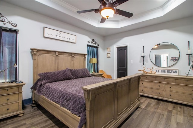 bedroom featuring ornamental molding, a tray ceiling, dark wood-style flooring, and a ceiling fan