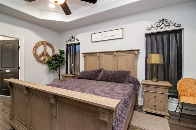 bedroom featuring ceiling fan, a tray ceiling, dark wood-type flooring, and ornamental molding