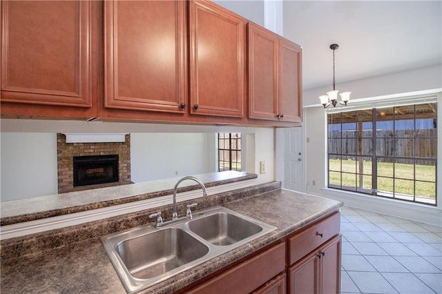 kitchen featuring pendant lighting, light tile patterned floors, dark countertops, a brick fireplace, and a sink