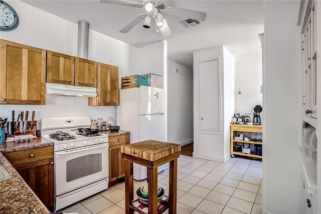 kitchen with white appliances, brown cabinetry, light tile patterned flooring, and under cabinet range hood