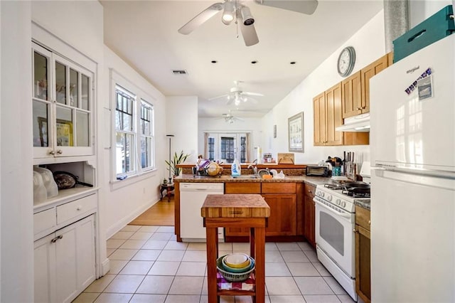 kitchen featuring a peninsula, white appliances, light tile patterned flooring, and under cabinet range hood