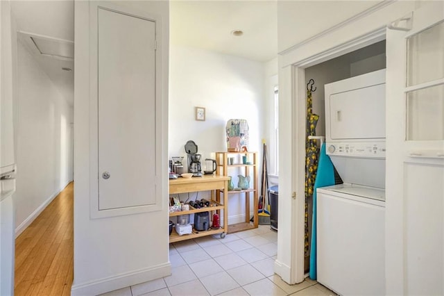 clothes washing area featuring laundry area, light tile patterned floors, baseboards, and stacked washer and clothes dryer