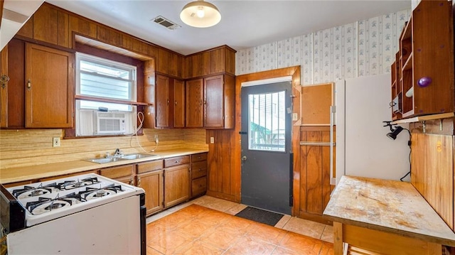 kitchen with wallpapered walls, visible vents, brown cabinets, white gas range, and a sink