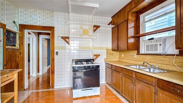 kitchen with brown cabinetry, light tile patterned flooring, a sink, and gas range