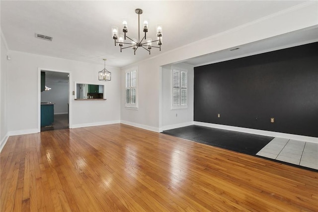 spare room featuring a chandelier, wood-type flooring, visible vents, and baseboards