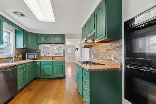 kitchen featuring visible vents, green cabinetry, stainless steel appliances, under cabinet range hood, and a sink