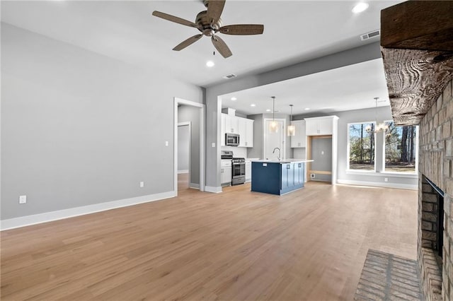 unfurnished living room with baseboards, light wood-style floors, a brick fireplace, a sink, and ceiling fan with notable chandelier