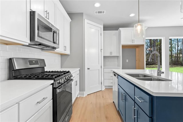 kitchen featuring visible vents, white cabinets, blue cabinets, stainless steel appliances, and a sink