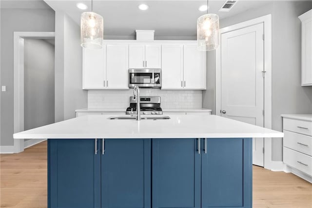 kitchen with stainless steel microwave, a sink, visible vents, and blue cabinets