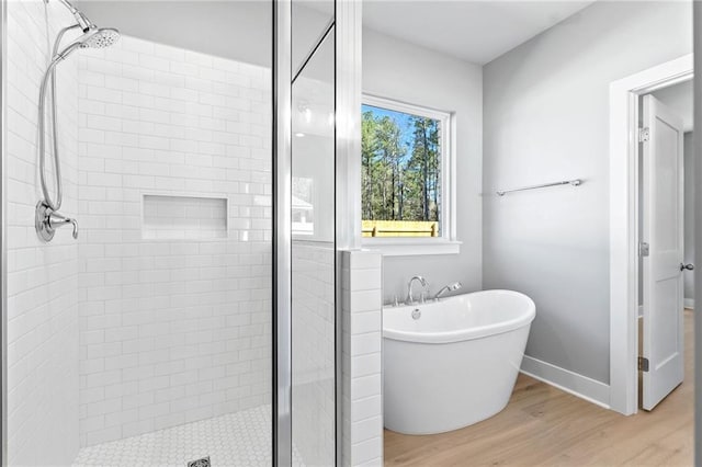 full bathroom featuring a stall shower, a freestanding bath, baseboards, and wood finished floors