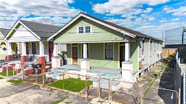 view of front of house with a fenced front yard, a gate, a porch, and roof with shingles