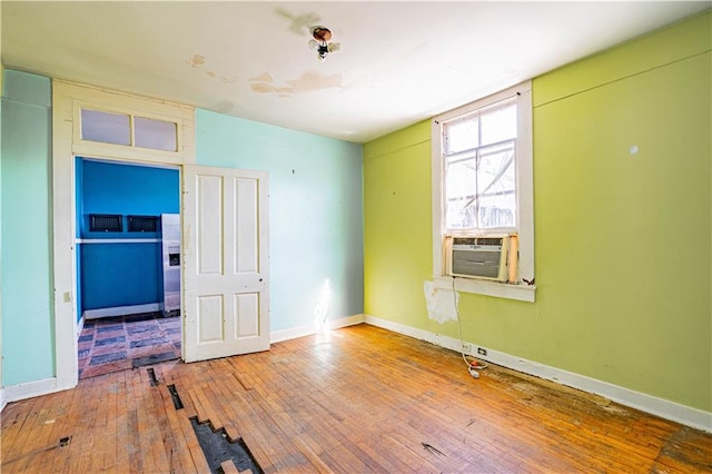 unfurnished room featuring cooling unit, hardwood / wood-style flooring, and baseboards