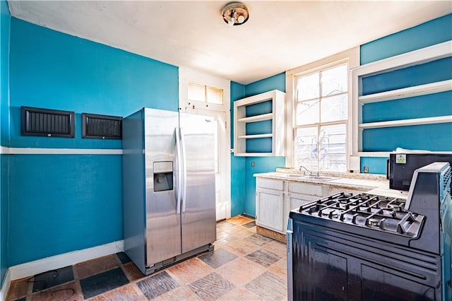 kitchen with open shelves, baseboards, light countertops, stone finish flooring, and stainless steel fridge