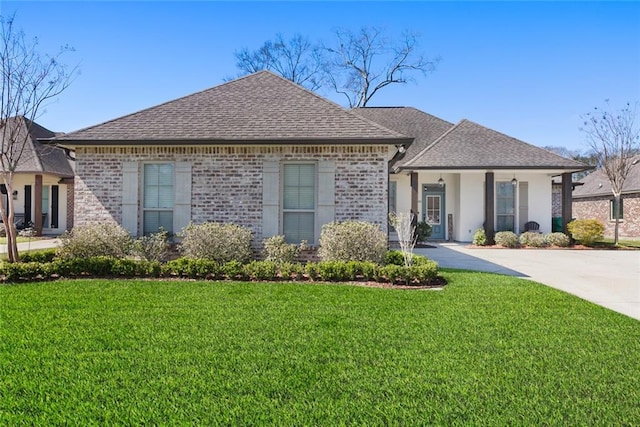 french country home featuring brick siding, a front lawn, and roof with shingles