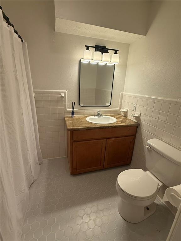 full bathroom with tile walls, toilet, wainscoting, vanity, and tile patterned flooring