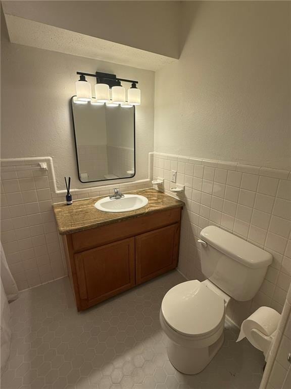 bathroom with a wainscoted wall, toilet, tile walls, and vanity